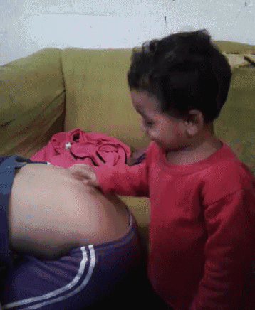a little girl in a red shirt is touching a woman 's belly