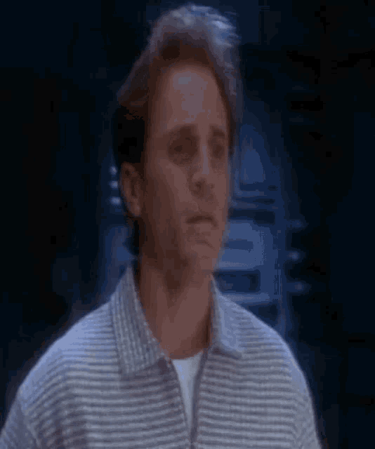 a man in a striped shirt is looking at the camera with a serious look on his face .