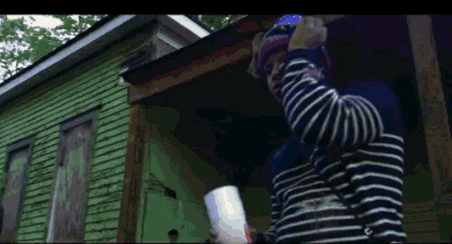a man in a striped shirt is standing on a porch holding a cup