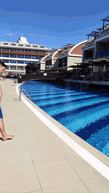 a man standing next to a large swimming pool with a hotel in the background