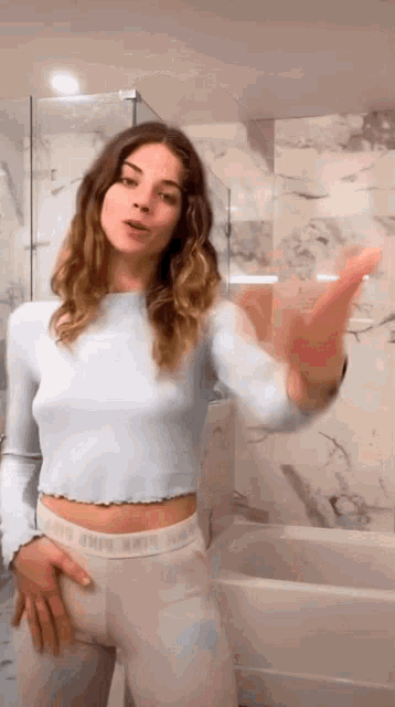 a woman in a blue sweater and white pants is standing in a bathroom