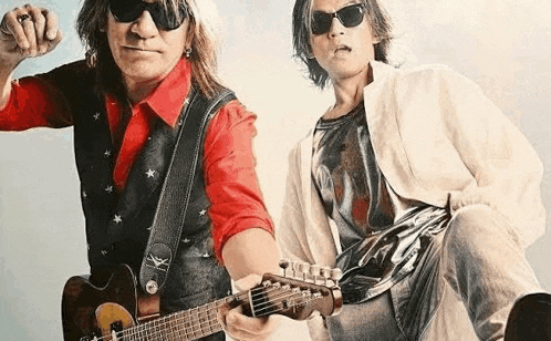 two men are standing next to each other playing guitars .
