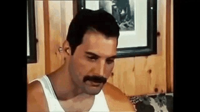 a man with a mustache is sitting on a couch in a room .