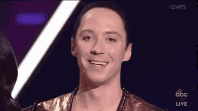 a man is smiling on a stage while wearing a gold top .