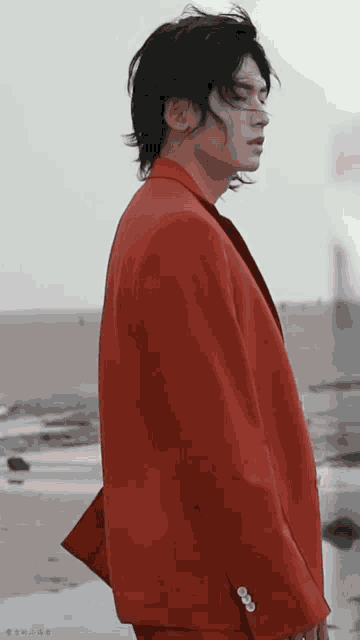 a man in a red suit is standing in front of the ocean .