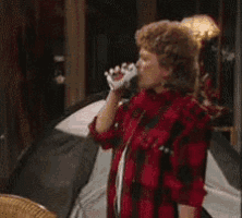 a woman in a red and black plaid shirt is drinking from a glass .