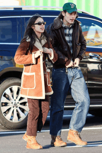 a man wearing a green hat with the letter p on it walks with a woman