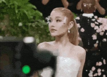 a woman in a white dress is standing in front of a camera and looking at the camera .