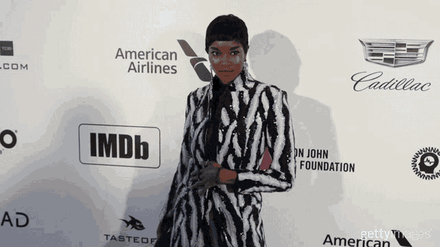 a woman stands on a red carpet sponsored by american airlines and imdb
