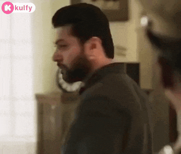 a man with a beard is standing in a room with a clock on the wall .