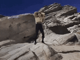a man is standing on top of a rocky hill with his arms outstretched