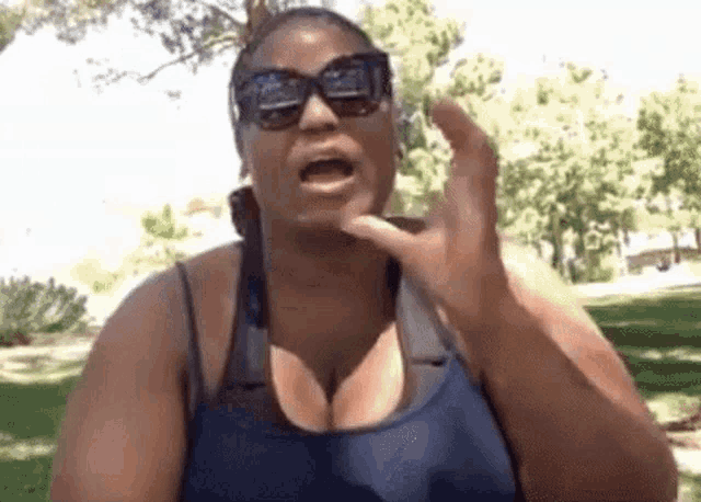 a woman wearing sunglasses and a blue tank top is giving a thumbs up .