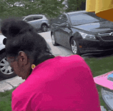 a woman in a pink shirt is looking over her shoulder at a black car