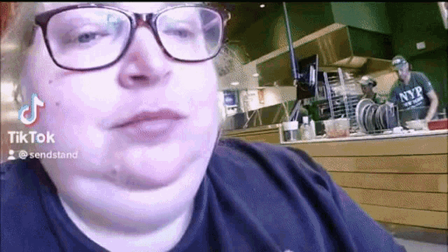 a woman wearing glasses and a nyp shirt is sitting in front of a counter