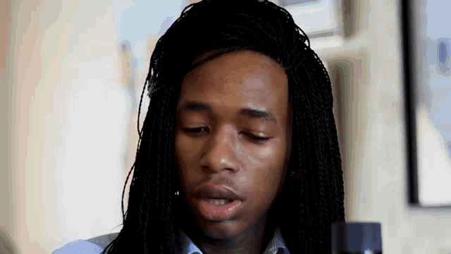 a young man with long braided hair is looking down at something .