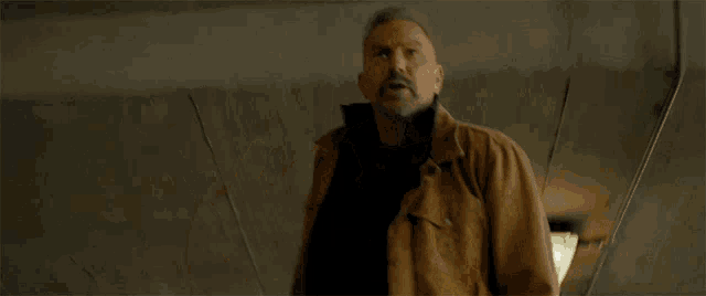 a man with a beard wearing a brown jacket looks up