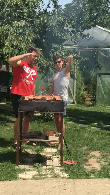 a man in a red shirt with a white x on it stands next to a woman cooking on a grill