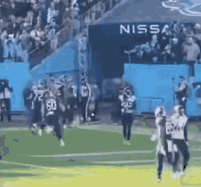 a group of football players are running on a field with a nissan sign in the background .