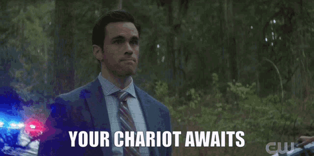 a man in a suit and tie says " your chariot awaits " while standing in the woods