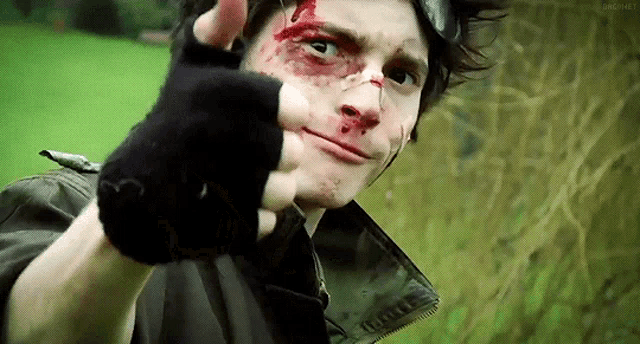 a man with blood on his face is pointing at the camera