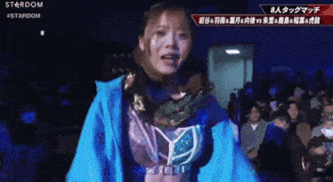 a woman in a blue jacket stands in front of a crowd with the word stardom on the screen