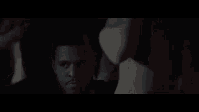 a man is sitting in a dark room with a woman standing next to him .