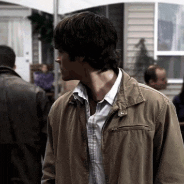a man in a brown jacket is standing in front of a house