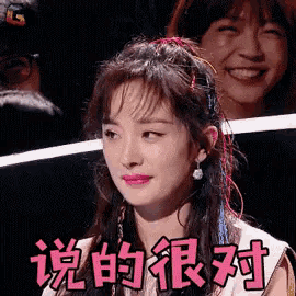 a woman with chinese writing on her face is smiling while sitting in front of a crowd .