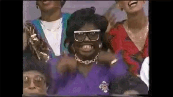 a group of people are standing around a woman wearing glasses and a purple shirt .