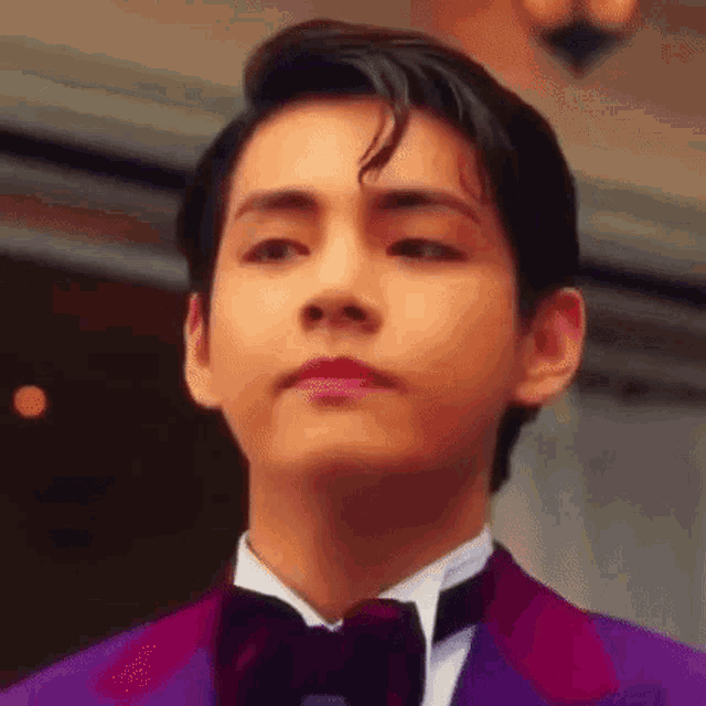 a close up of a young man wearing a purple suit and bow tie .