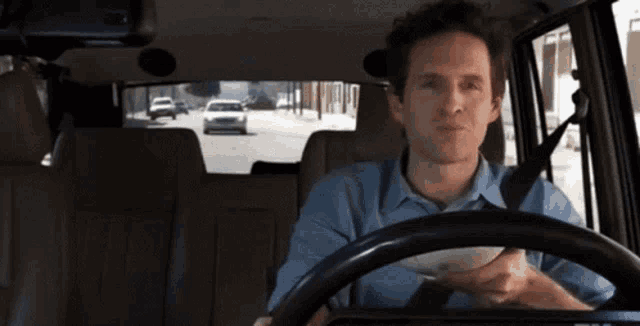 a man in a blue shirt is driving down a street