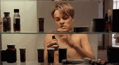 a shirtless man is smoking a cigarette in front of a medicine cabinet filled with bottles of pills .