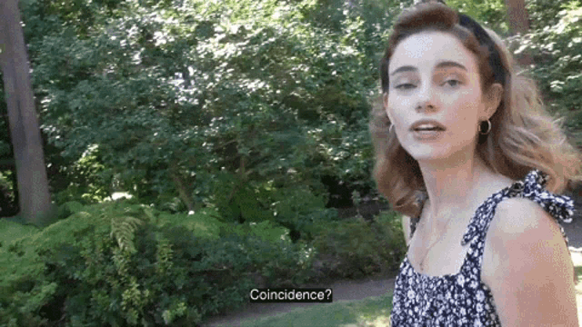 a woman in a black and white dress is standing in a park with trees in the background and says coincidence .