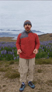a man in a red shirt stands in front of a field of blue flowers
