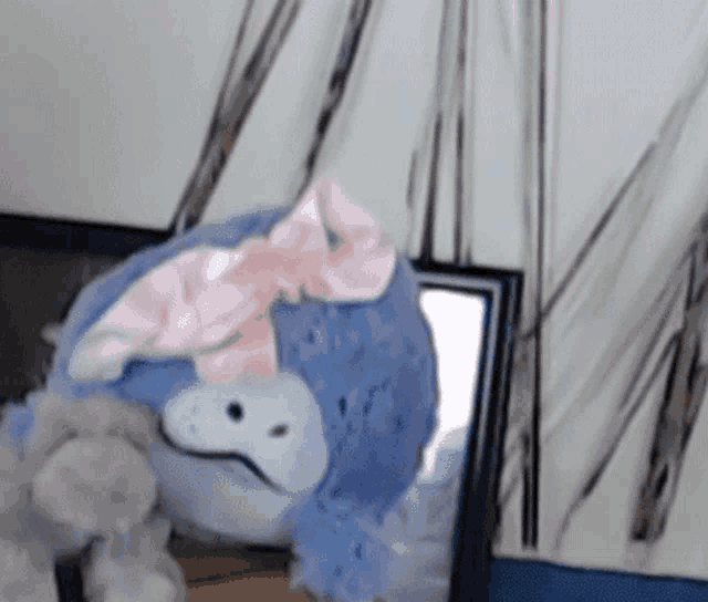 a blue stuffed animal with a pink bow on its head is sitting in front of a mirror