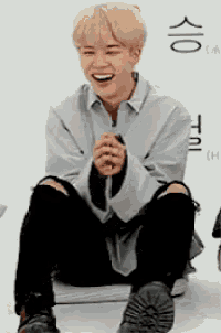 a young man with blonde hair is sitting on the floor with his hands folded and smiling