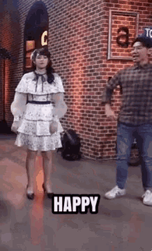 a woman in a white dress is standing next to a man in a plaid shirt and says happy .