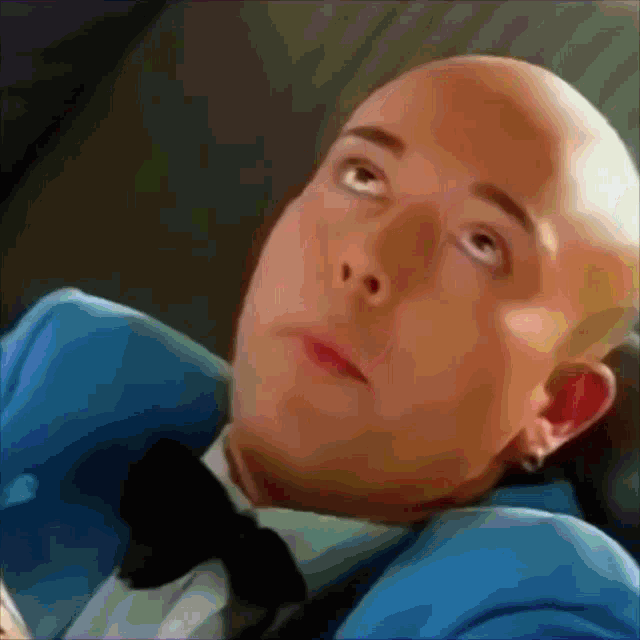 a bald man wearing a blue suit and bow tie looks up