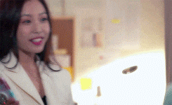 a woman in a white suit is smiling while holding a bottle of wine in her hand .