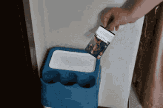 a person is putting a cigarette in a blue trash can
