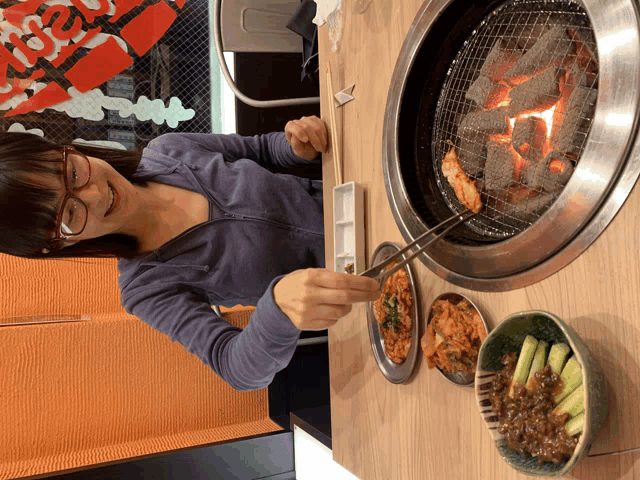 a woman sitting at a table with plates of food in front of a grill with a sign that says ' beef '