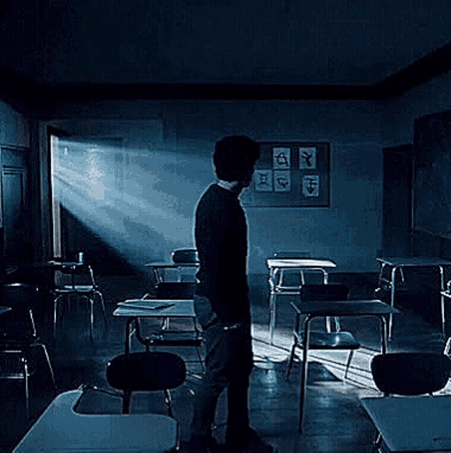 a man stands in a dark classroom with a bulletin board with drawings on it that says " a "