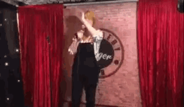 a woman is standing on a stage in front of a red curtain holding a microphone .