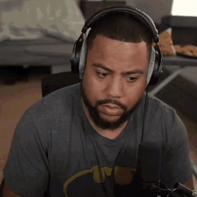 a man with a beard is wearing headphones and a batman shirt while sitting in front of a microphone .