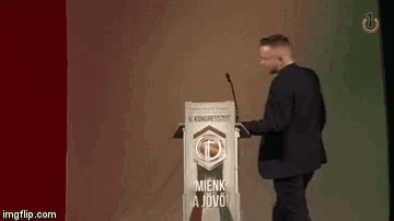 a man in a suit and tie is standing at a podium and saying i 'm the boss