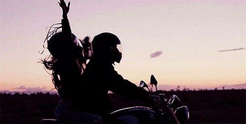 a man and a woman riding a motorcycle at sunset
