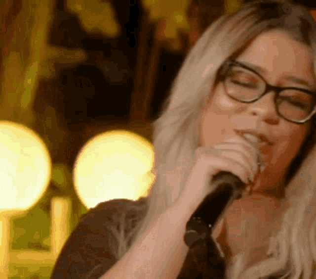 a woman wearing glasses is singing into a microphone in a dark room .