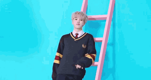 a young man in a sweater and tie is leaning against a pink ladder against a blue background .
