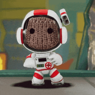 a knitted character wearing a helmet and headphones is holding a camera