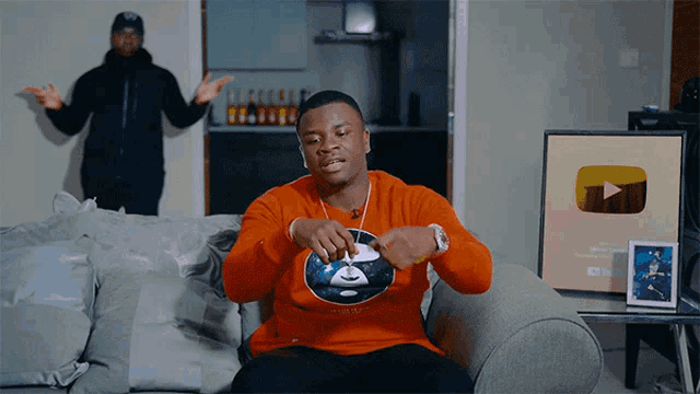 a man sitting on a couch wearing an orange sweatshirt that says " a bathing ape " on it